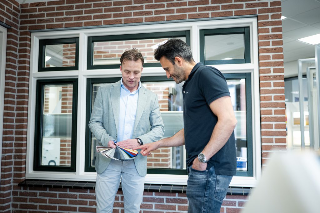 Multi Kozijn collega staat in de showroom en laat kleuropties voor kunststof kozijnen zien aan klant